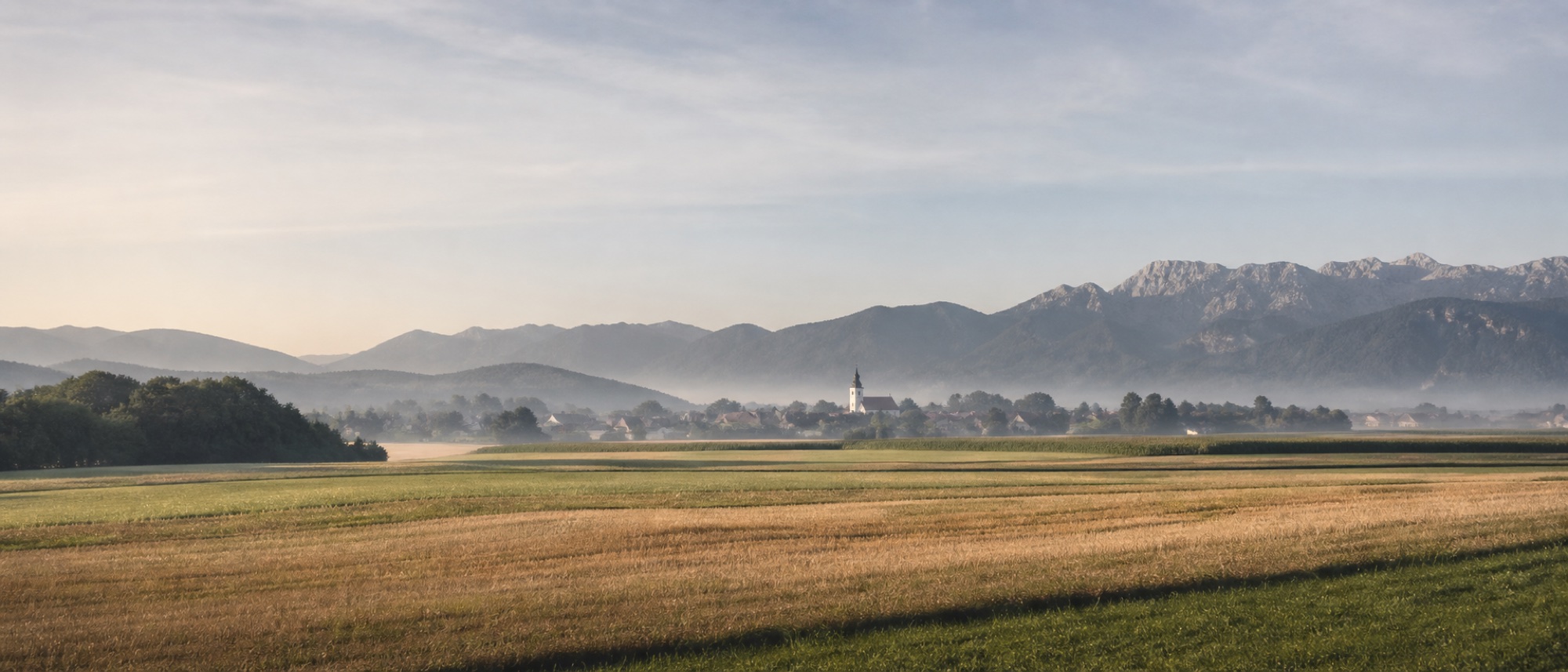 Ilustrativni panoramski motiv vodiških polj, vasi in Kamniško-Savinjskih Alp.